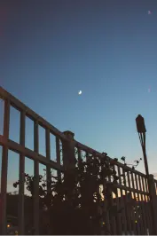 a crescent moon during sunset with a white fence